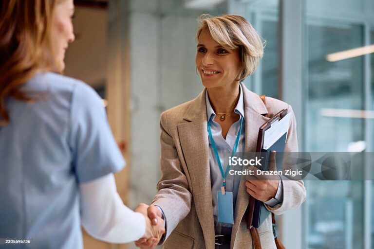 Happy businesswoman handshaking with female nurse at medical clinic.